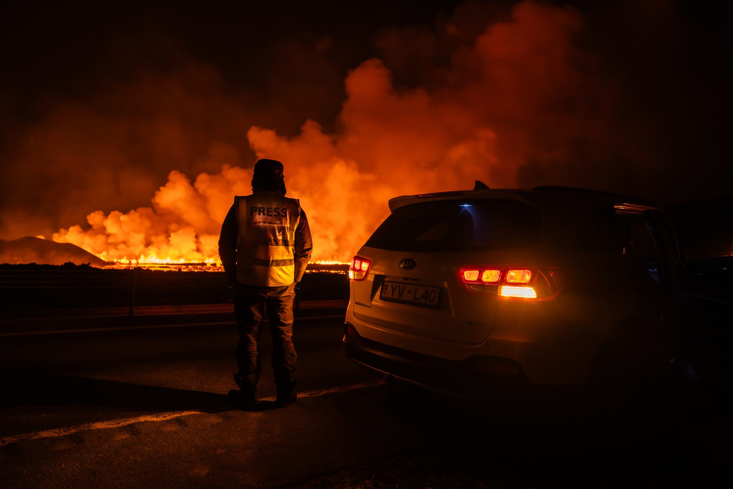 Press-credentialed photographer watching a roadside Sundhnúkur lava flow at night in Iceland.
