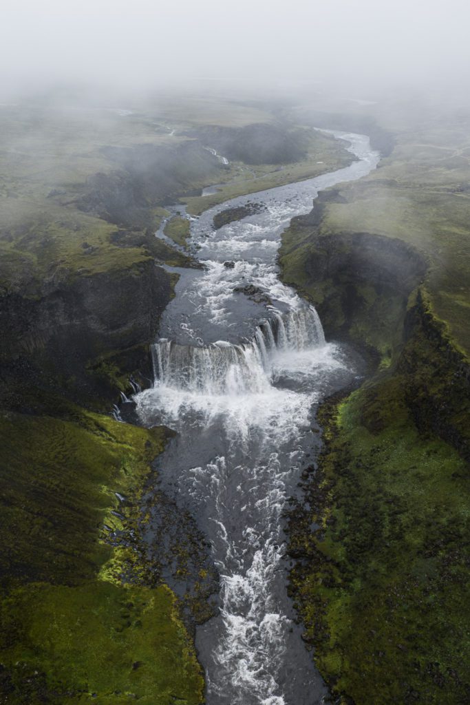 Aerial drone shot of a waterfall and braided river through a moody canyon in the Icelandic Highlands.