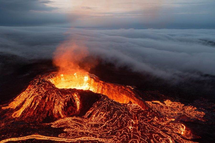Aerial of a Fagradalsfjall cone smoking above a sea of clouds with lava channels below.