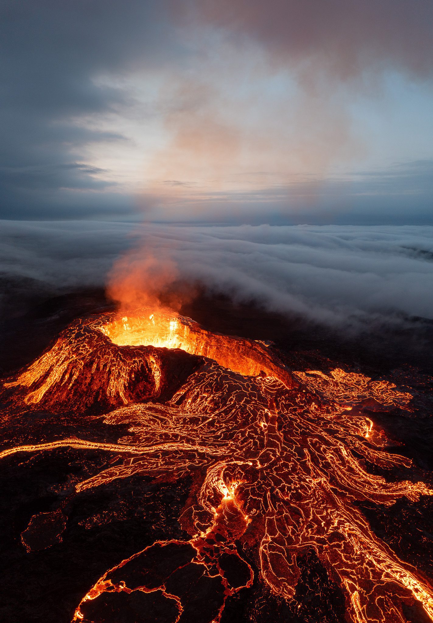 Aerial of a Fagradalsfjall cone smoking above a sea of clouds with lava channels below.