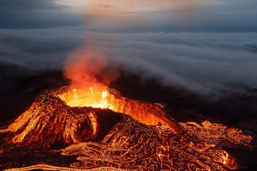 Aerial drone view of an erupting crater rising above a sea of clouds.
