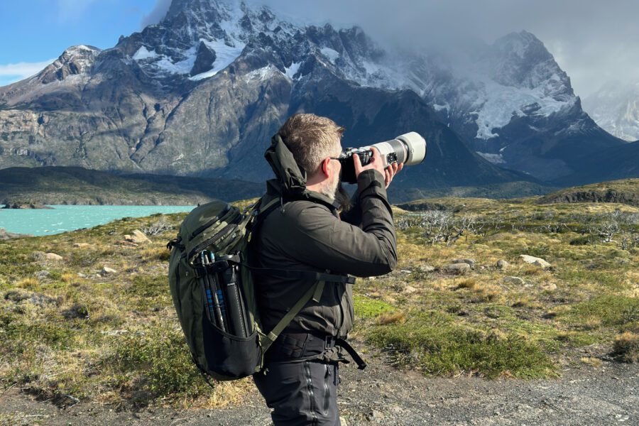 Photographer using the Canon RF 100-500mm on the trail with the Cuernos del Paine in Patagonia behind.