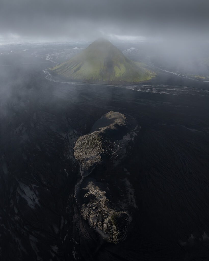 Aerial drone shot of Mælifell rising from a black sand desert under stormy clouds in the Icelandic Highlands.