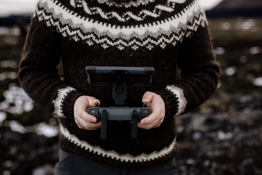Hands holding a DJI Mavic 4 Pro controller in an Icelandic lopapeysa sweater in the Highlands.